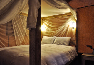 Cama cómoda con mosquitera e iluminación cálida en SunLodge Bintulu en Camping Village Poljana, Croacia.