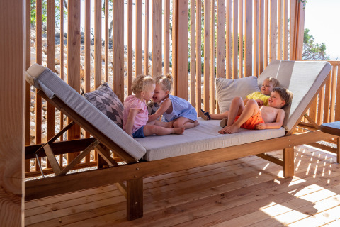 Cuatro niños juegan y descansan en una tumbona de madera en SunLodge Catalpa, Camping Village Poljana, Croacia.