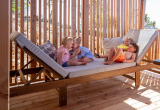 Cuatro niños juegan y descansan en una tumbona de madera en SunLodge Catalpa, Camping Village Poljana, Croacia.