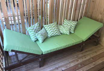 Groene ligstoel met sierkussens in houten hut bij SunLodge Catalpa, Camping Village Poljana, Kroatië.