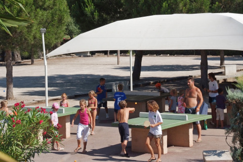 Niños y adultos juegan al ping-pong bajo una carpa en un parque vacacional de Provenza-Alpes-Costa Azul, Francia.