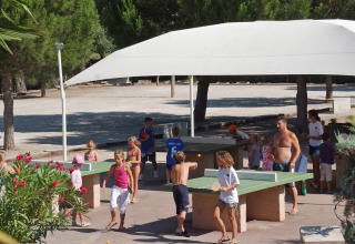 Niños y adultos juegan al ping-pong bajo una carpa en un parque vacacional de Provenza-Alpes-Costa Azul, Francia.
