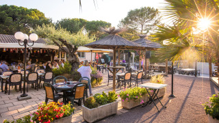 Zona exterior para comer en Camping Leï Suves, Provenza, con comensales, flores y luz del atardecer.
