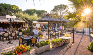 Zona exterior para comer en Camping Leï Suves, Provenza, con comensales, flores y luz del atardecer.
