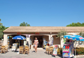 Butik og udendørs café ved Camping Leï Suves i Provence, Frankrig, med parasoller og solrigt vejr.