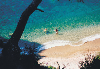 Two people swim in clear blue water near the shore at Camping Leï Suves holiday park in southern France.
