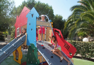 Tres niños juegan en un colorido parque infantil con tobogán y muro de escalada en Camping Leï Suves, Francia.