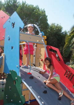 Tres niños juegan en un colorido parque infantil con tobogán y muro de escalada en Camping Leï Suves, Francia.