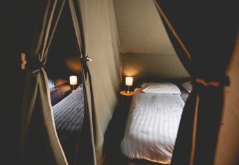 Innenraum eines Luxury Lodgetents mit gemütlichem Bett und Lampen auf Camping de Bovenberg in den Niederlanden.