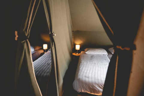 Interior of a Luxury Lodgetent with a cozy bed and lamps at Camping de Bovenberg, Netherlands, softly lit.