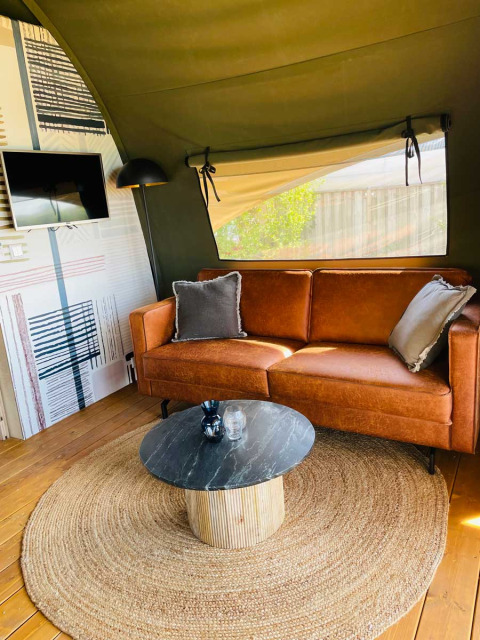 Interior de tienda de lujo en Camping de Bovenberg, Países Bajos, con sofá marrón y decoración moderna.
