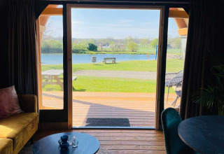 Vista desde una tienda lodge de lujo en Camping de Bovenberg, Países Bajos, con terraza y lago al fondo.