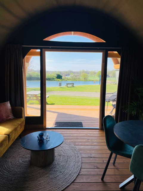 Vue depuis une tente lodge de luxe au Camping de Bovenberg aux Pays-Bas, terrasse et lac à l'horizon.