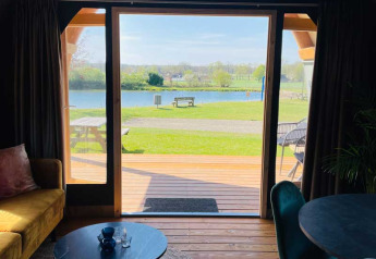 Vue depuis une tente lodge de luxe au Camping de Bovenberg aux Pays-Bas, terrasse et lac à l'horizon.