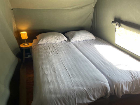 Zwei Einzelbetten mit weißer Bettwäsche und Nachtlampe in einem Luxus-Safarizelt bei Camping de Bovenberg.