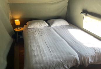 Dos camas individuales con sábanas blancas y lámpara en tienda safari de lujo en Camping de Bovenberg, Países Bajos.