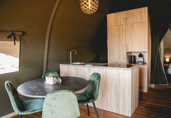 Cocina moderna y mesa de comedor con sillas verdes en una tienda safari de lujo en Camping de Bovenberg, Países Bajos.