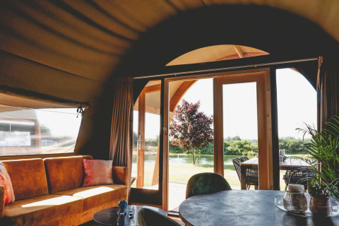 Vista interna di una tende safari di lusso al Camping de Bovenberg, con divano e terrazza nei Paesi Bassi.