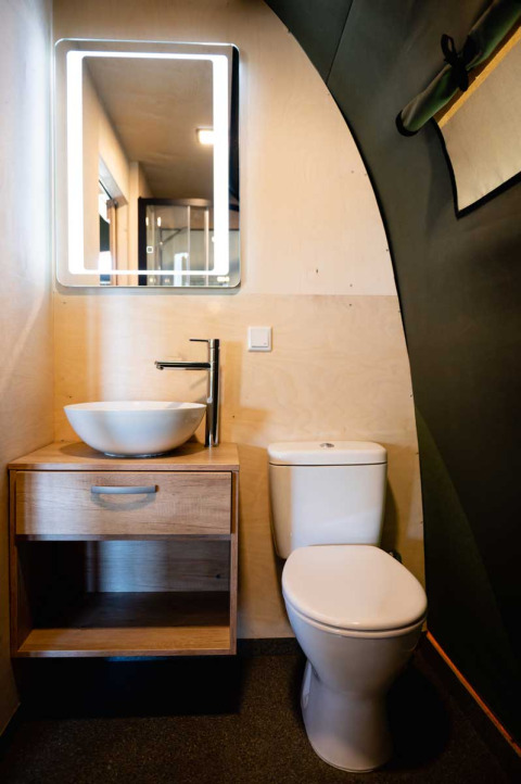 Stijlvolle badkamer in luxe safaritent met ronde waskom, houten kast, spiegel met verlichting en toilet.