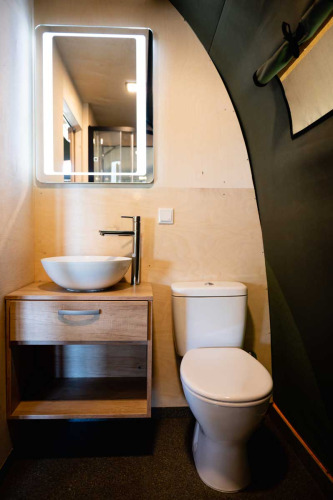 Salle de bain moderne sous tente de luxe avec vasque, meuble en bois, miroir éclairé et toilettes.