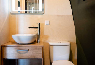 Moderne badeværelse med skålformet vask, trækabinet, indrammet spejl og toilet i luksustelt.