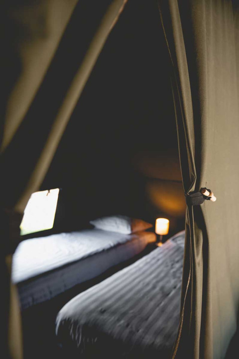 Innenraum eines luxuriösen Safarizelts mit zwei Betten und warmem Licht bei Camping de Bovenberg, Niederlande.