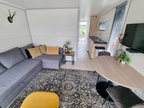 Salón moderno en apartamento vacacional con sofá gris, mesa redonda y cocina en Marina Parcs, Norte de Holanda.