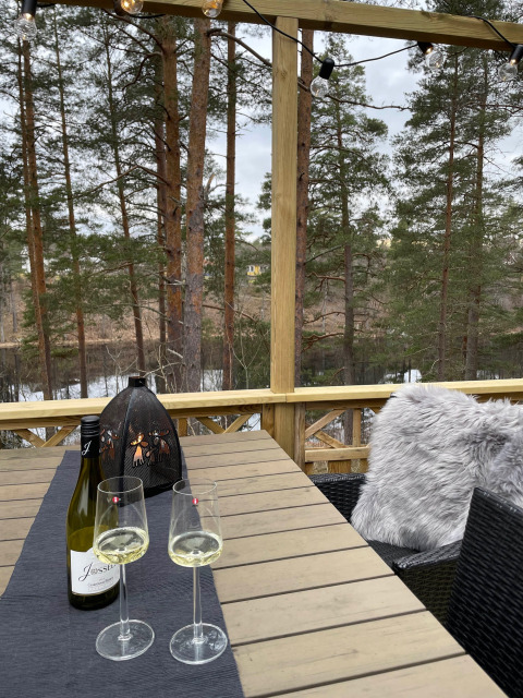 Buitentafel met wijn en glazen in Småland Miniglamping, Kalmar län, Zweden, tussen de bomen.