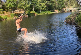 A boy swings over a lake on a rope at Småland Miniglamping, a holiday park in Kalmar län, Sweden.