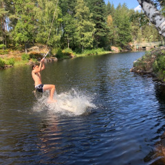 Un chico se balancea sobre un lago con una cuerda en Småland Miniglamping, parque vacacional en Kalmar län, Suecia.