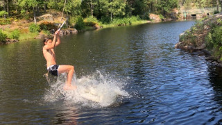 Un chico se balancea sobre un lago con una cuerda en Småland Miniglamping, parque vacacional en Kalmar län, Suecia.
