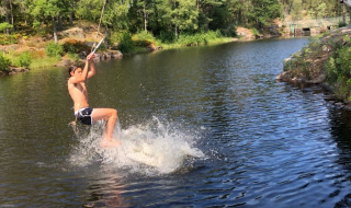 Un chico se balancea sobre un lago con una cuerda en Småland Miniglamping, parque vacacional en Kalmar län, Suecia.