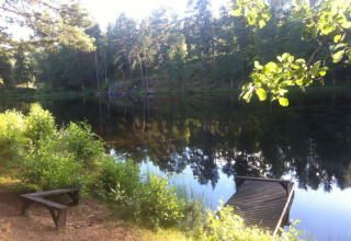 Sunny view of a calm lake with a small dock and bench at Småland Miniglamping, Kalmar län, Sweden.