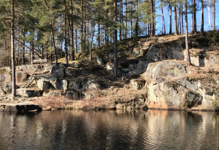 Rotsachtige oever met houten trap en dennenbomen bij Småland Miniglamping, Kalmar län, Zweden.