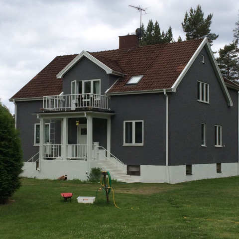 Villa gris moderna con techo de tejas rojas y balcón, rodeada de césped en Småland Miniglamping, Kalmar, Suecia.