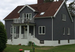 Villa gris moderna con techo de tejas rojas y balcón, rodeada de césped en Småland Miniglamping, Kalmar, Suecia.