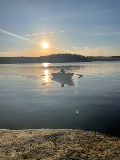Persona remando en un bote sobre un lago tranquilo al atardecer cerca de Gullringen, Kalmar län, Suecia.
