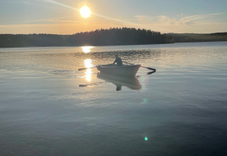 Eine Person rudert in einem Boot bei Sonnenuntergang auf einem ruhigen See nahe Gullringen, Kalmar län, Schweden.