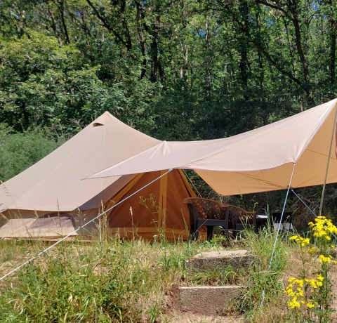 Tenda safari Belltent nella foresta, con tenda da sole, sedie all’aperto e fiori selvatici vicini.