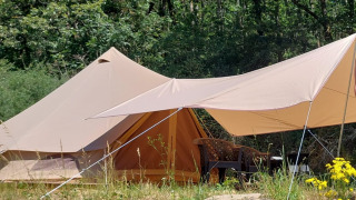 Tenda safari Belltent nella foresta, con tenda da sole, sedie all’aperto e fiori selvatici vicini.