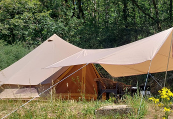 Tenda safari Belltent nella foresta, con tenda da sole, sedie all’aperto e fiori selvatici vicini.