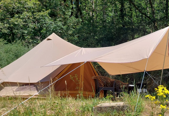 Tienda safari Belltent en un bosque, con toldo y sillas al aire libre rodeadas de flores silvestres.