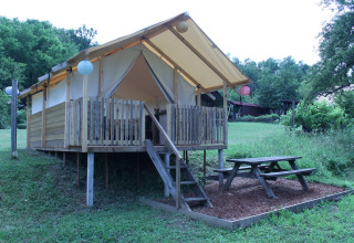 Tenda safari al Camping Sretanwolf in Croazia, veranda in legno rialzata e tavolo da picnic nel verde.