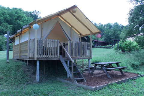 Tenda safari al Camping Sretanwolf in Croazia, veranda in legno rialzata e tavolo da picnic nel verde.