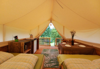 Interior de la tienda Safari en Camping Sretanwolf, Croacia, con camas, mesa de comedor y terraza.