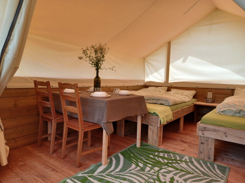 Interior de una tienda safari en Camping Sretanwolf en Croacia, con muebles de madera, camas y mesa.