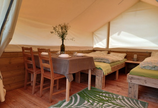 Interior de una tienda safari en Camping Sretanwolf en Croacia, con muebles de madera, camas y mesa.