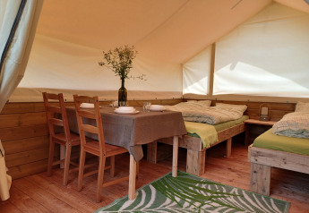 Interior de una tienda safari en Camping Sretanwolf en Croacia, con muebles de madera, camas y mesa.