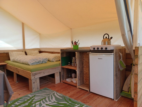 Interior de una tienda safari en Camping Sretanwolf, Croacia, con cama y cocina pequeña equipada.