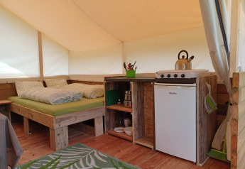 Interior de una tienda safari en Camping Sretanwolf, Croacia, con cama y cocina pequeña equipada.